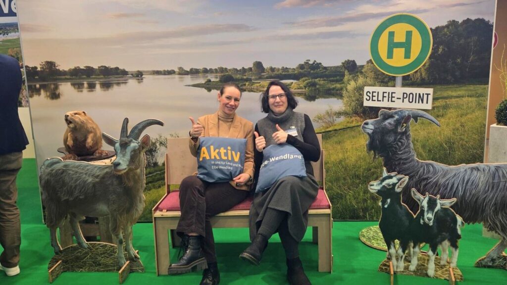 Zwei Personen auf einer Bank zwischen Ziegen-Aufstellern aus Holz