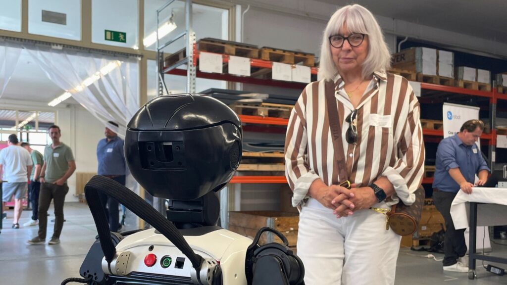 Humanoider Roboter UMe und Mitarbeiterin der Wirtschaftsförderung Wendland.Elbe stehen sich in einer Lggerhalle gegenüber.